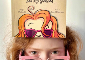 Praca Łucji Kłosińskiej: Łucja wcieliła się w bohaterkę książki Megan McDonald- Hanię Humorek. Zdjęcie przedstawia dziewczynkę z rozpuszczonymi, rudymi włosami, w dużych różowych okularach.